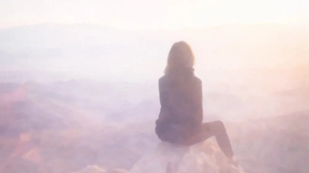 霧がかった幻想的な山頂で、一人の女性が静かに景色を眺める後ろ姿。内向型が自分らしくウェルビーイングを追求するイメージ。